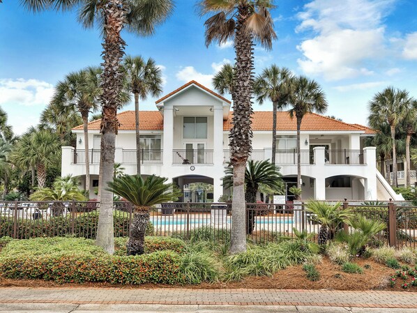 A two-story white building with a red-tiled roof, surrounded by palm trees and a swimming pool.