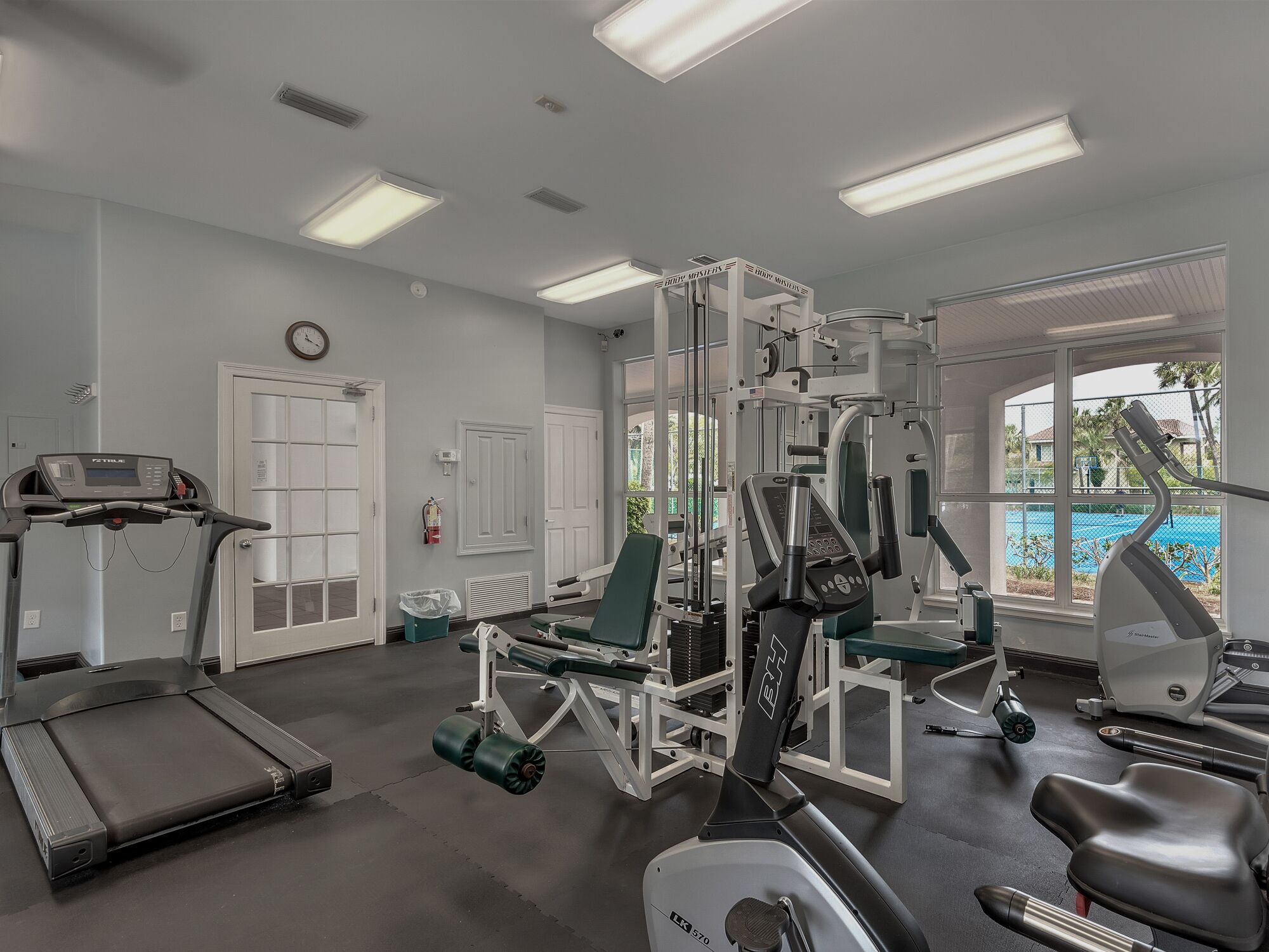 A gym with exercise equipment, a treadmill, and a window with a view of a pool.