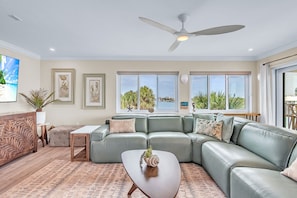 A living room with a sectional sofa, a coffee table, a ceiling fan, and large windows with a view.