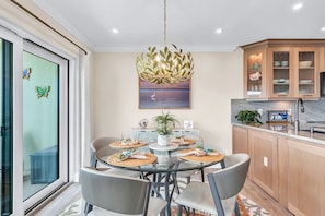 A modern kitchen with a glass dining table, wooden cabinets, and a decorative chandelier.