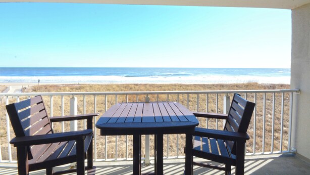 A balcony with a table and two chairs overlooking a beach. - Spacious, impeccably-styled 1 bedroom oceanfront condo with free WiFi and fabulous view of the ocean just steps to the beach! (Ocean City)