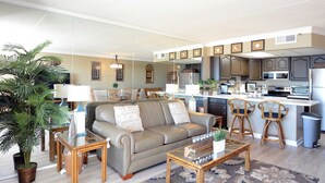 A modern living room with a sofa, coffee table, and chairs, a kitchen with a central island, and a dining area with chairs. - Spacious, impeccably-styled 1 bedroom oceanfront condo with free WiFi and fabulous view of the ocean just steps to the beach! (Ocean City)