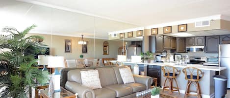 Un salon moderne comprenant un canapé, une table basse et des fauteuils, une cuisine avec un îlot central et un coin repas avec des chaises.