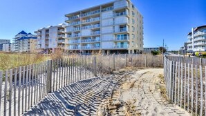 A multi-story building with balconies, a sandy path, and a wooden fence. - Spacious, impeccably-styled 1 bedroom oceanfront condo with free WiFi and fabulous view of the ocean just steps to the beach! (Ocean City)