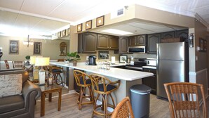 A modern kitchen with a central island, bar stools, a refrigerator, and a dining area with a sofa and chairs. - Spacious, impeccably-styled 1 bedroom oceanfront condo with free WiFi and fabulous view of the ocean just steps to the beach! (Ocean City)