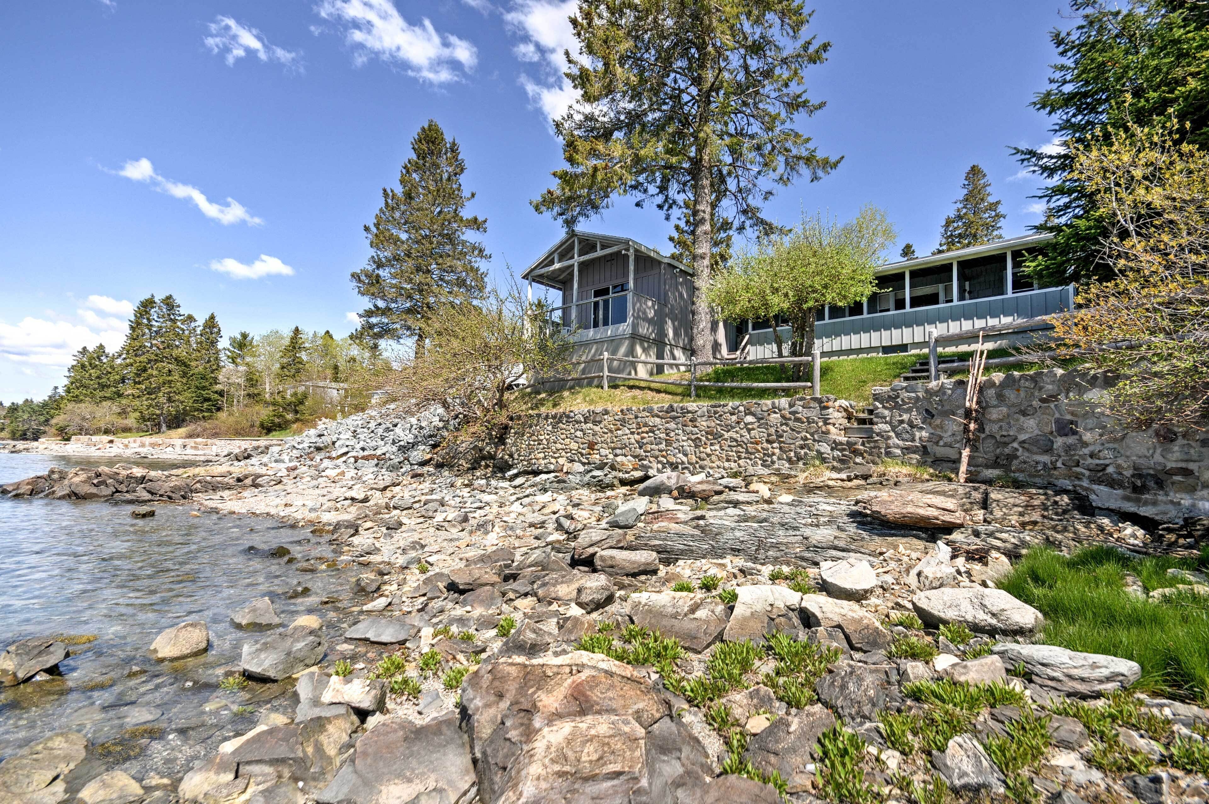 Una cabaña junto al lago con un muro de contención de piedra y una terraza de madera.
