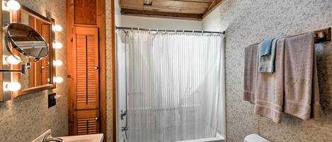 A bathroom with a wooden ceiling, a bathtub, a toilet, a sink, and a mirror with lights.
