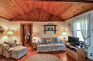 A cozy living room with wooden ceiling beams, a floral sofa, a television, and two lamps.