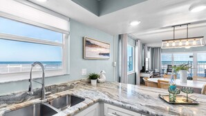 A kitchen with a large window, a sink, and a dining area with a view of the ocean.