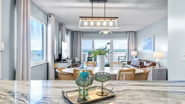 A modern hotel room with a dining area, a balcony with a view, and a ceiling fan.