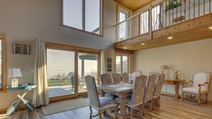 Een ruime eethoek met een houten tafel, gestoffeerde stoelen, grote ramen en uitzicht op het omliggende landschap.