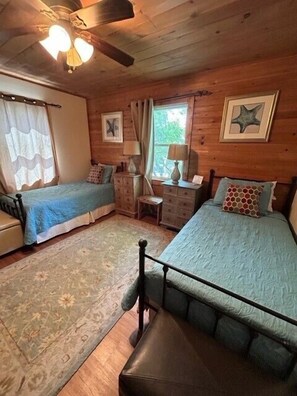 Een gezellig slaapkamer in chaletstijl met twee eenpersoonsbedden, een houten plafond en een klein bureau met stoel.