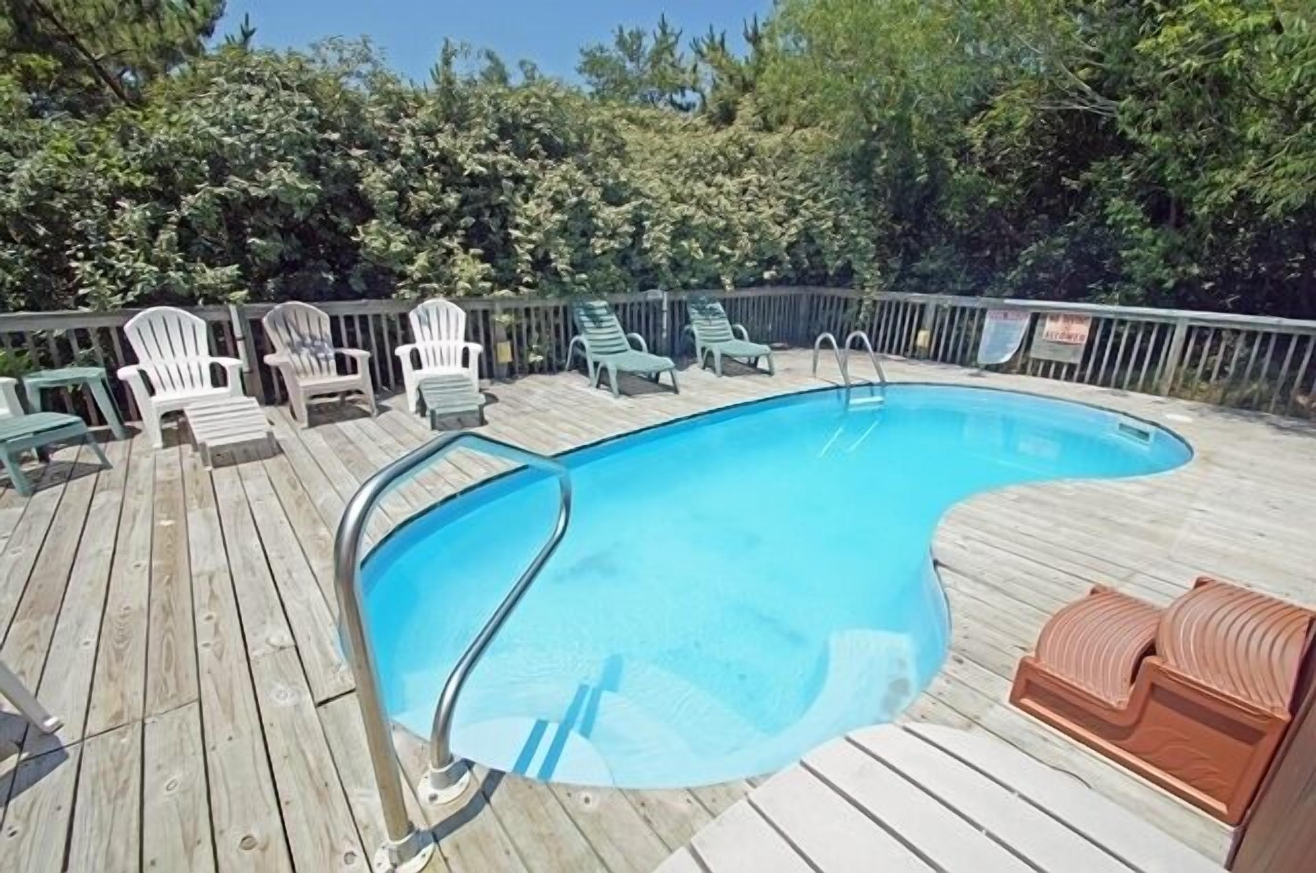 Una terraza de madera con piscina, rodeada de sillas verdes y una valla de madera.
