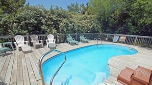 En træterrasse med en swimmingpool, omgivet af grønne stole og et træhegn.
