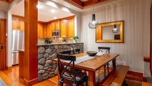 A modern kitchen with wooden cabinets, a stone backsplash, and a dining area with a wooden table and chairs.