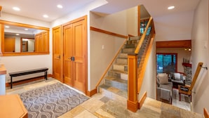 A spacious hallway with wooden doors, a bench, a patterned rug, and a staircase with stone steps.