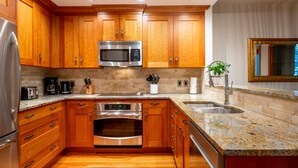 A modern kitchen with wooden cabinets, stainless steel appliances, granite countertops, and a built-in oven.