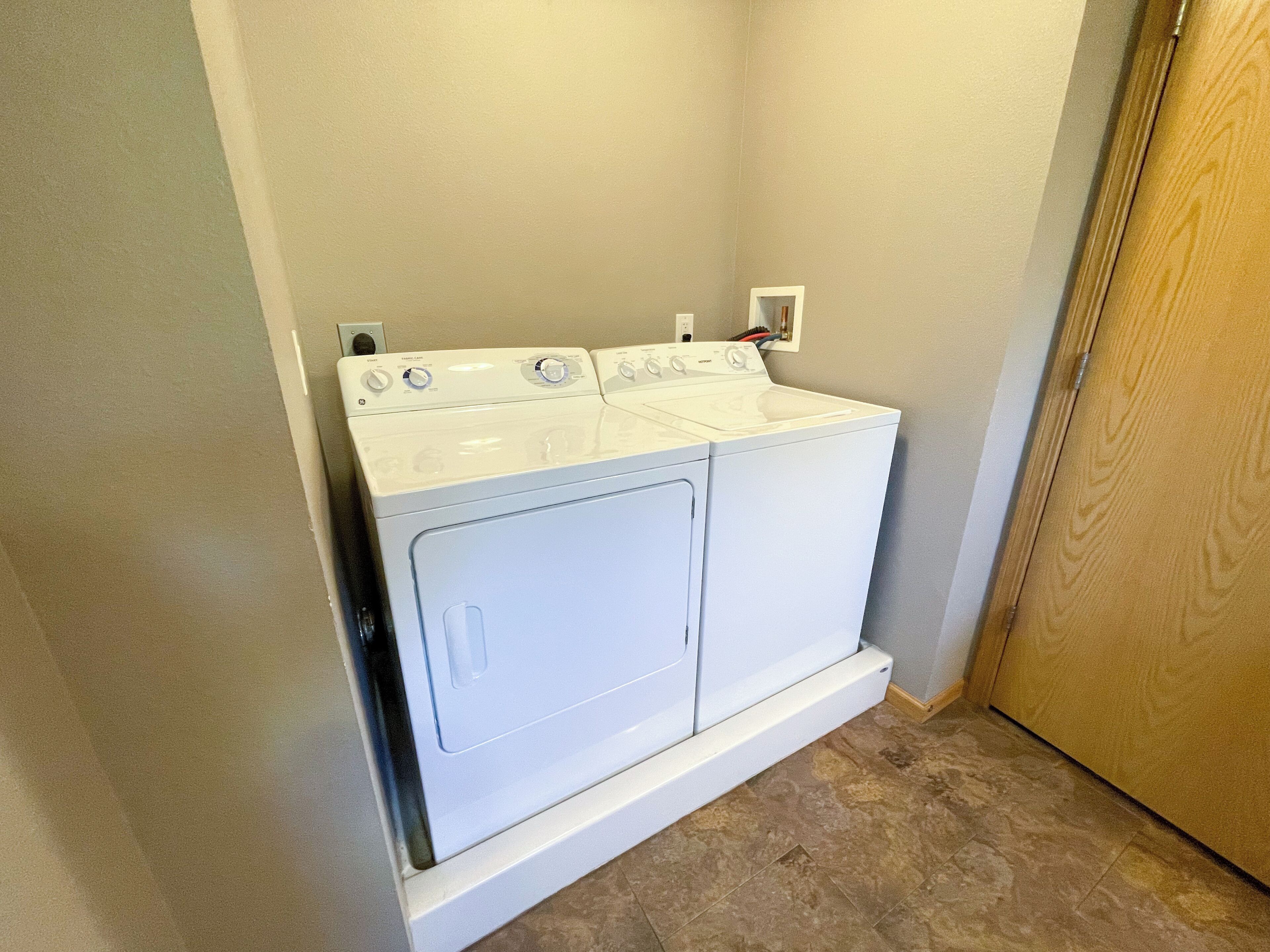 A front-loading washer and dryer unit in a laundry room with a tiled floor and a wooden door.