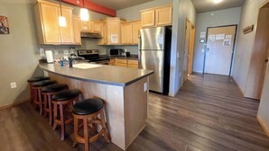 A modern kitchen with wooden cabinets, a stainless steel refrigerator, a built-in oven, and a bar area with stools. - Two Bedroom Condo @ Spring Brook Resort (Wisconsin Dells)