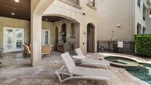 Un espacio exterior techado con sillones, piscina y un patio con cocina al fondo.