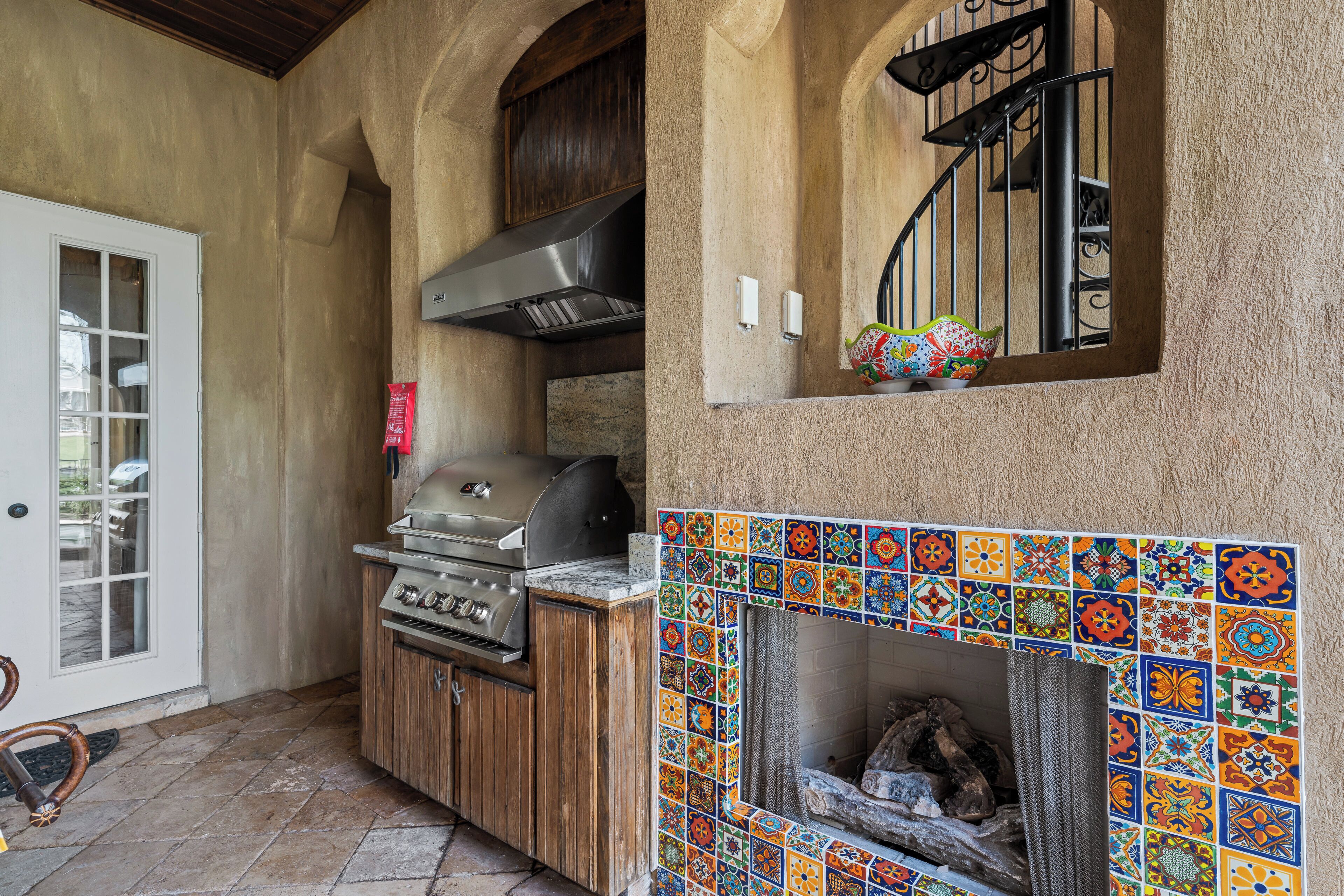 An outdoor kitchen area with a grill, a chimney, and a tiled fireplace.