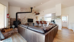 A modern living room with a fireplace, leather sofa, and a kitchen area in the background.