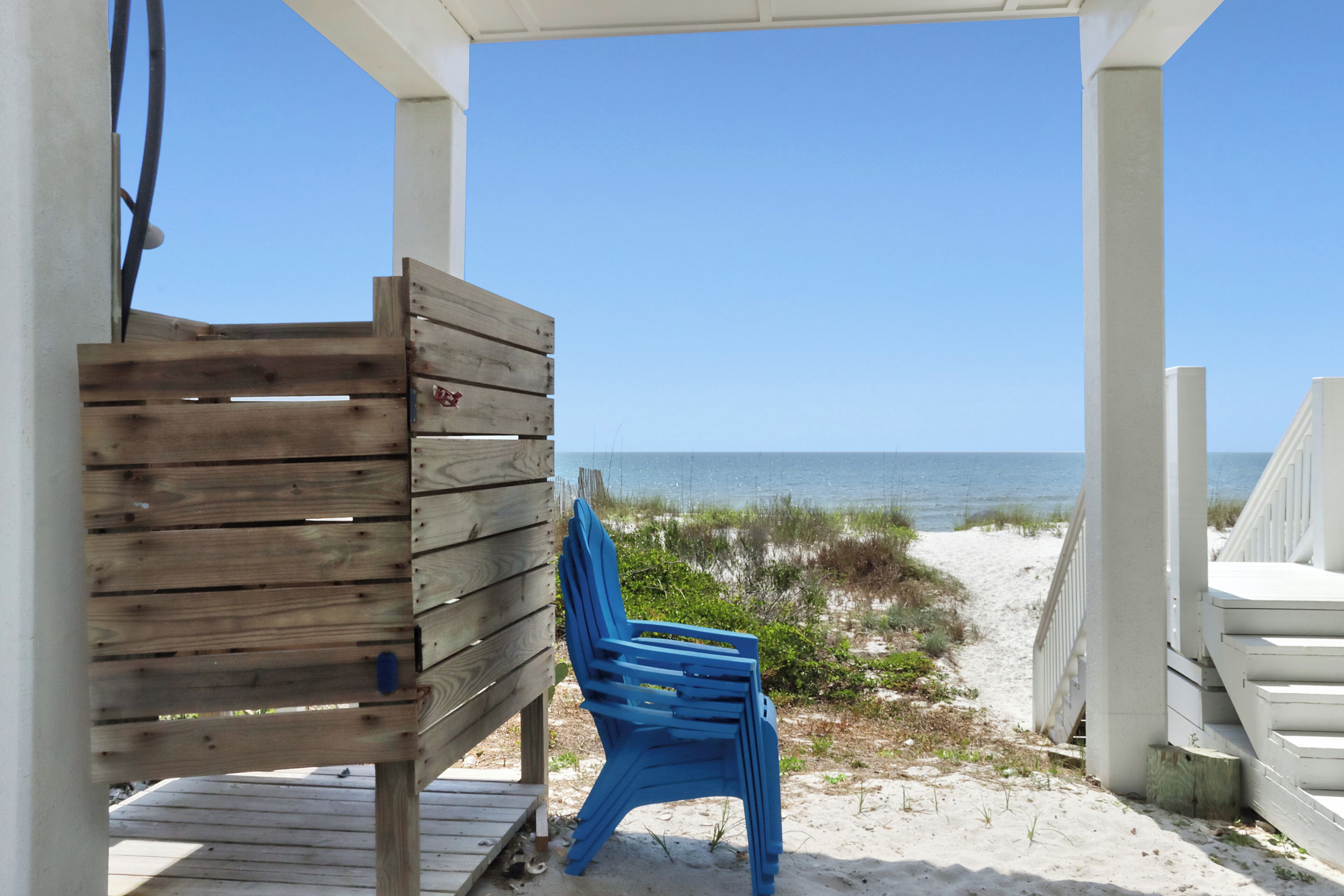 A wooden bench and a blue chair under a covered area with a view of the beach and ocean.