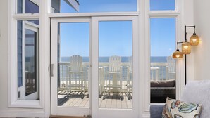 A room with a large sliding glass door leading to a deck with white chairs and a view of the ocean. - Sunroom, Quiet Neighborhood, Gulf Front, Private Dune Walkover ~ La Mer (Cape San Blas)