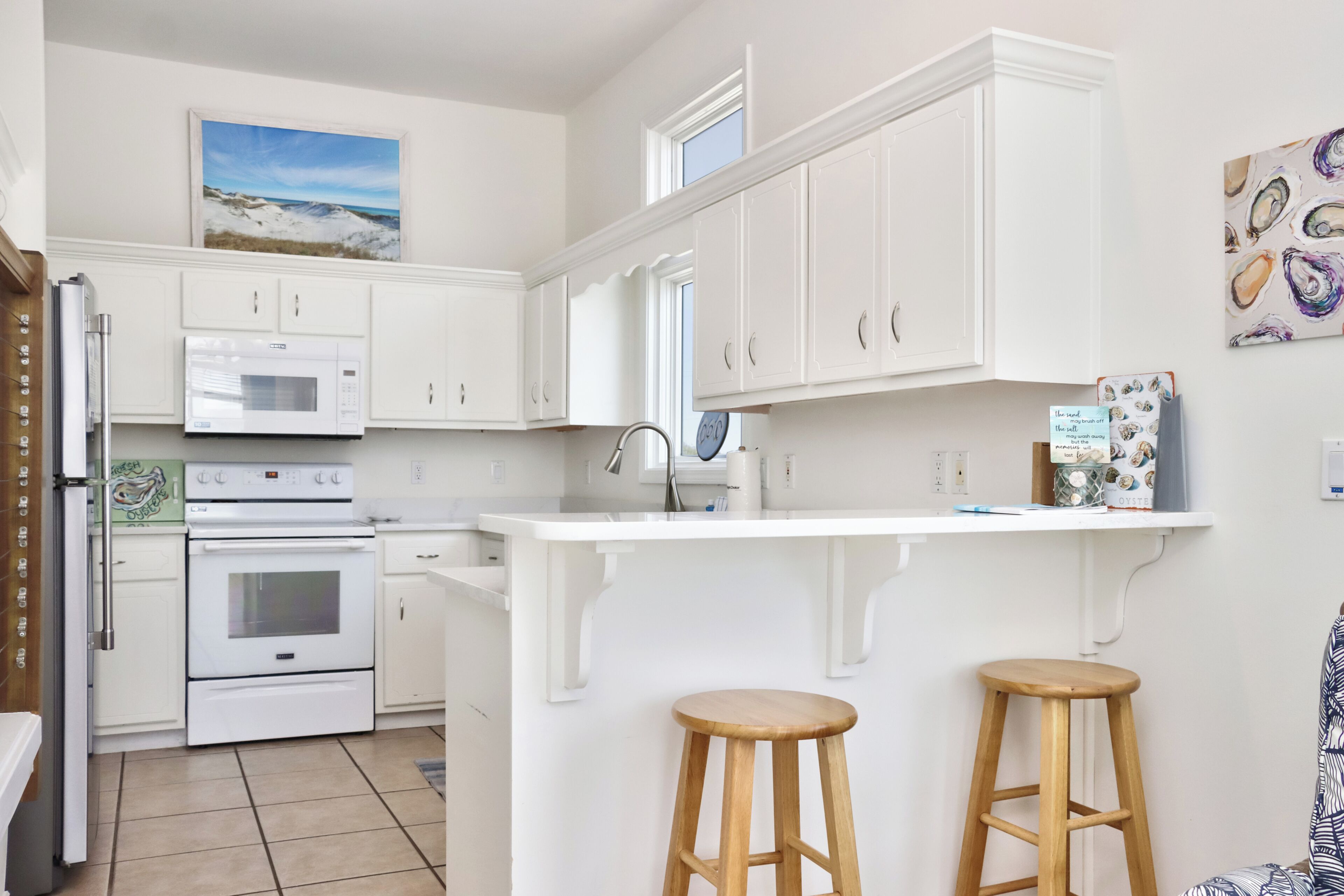 A kitchen with white cabinets, a microwave, an oven, and a bar area with stools.