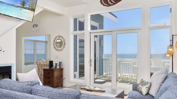 A spacious living room with a large TV, a fireplace, a balcony with outdoor furniture, and a view of the ocean. - Sunroom, Quiet Neighborhood, Gulf Front, Private Dune Walkover ~ La Mer (Cape San Blas)