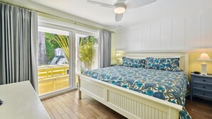 A bedroom with a bed, a ceiling fan, a nightstand, and a view of an outdoor area with a yellow deck and greenery.