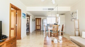 Un espacio habitable amplio con una mesa de centro de madera, un sofá y una mesa de comedor con sillas. Se aprecia una cocina al fondo con electrodomésticos modernos.