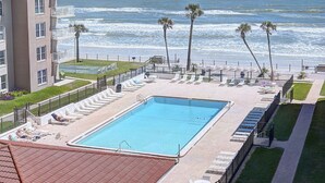 A pool area with a view of the ocean, surrounded by lounge chairs and palm trees. - Cute 2/2!Direct Oceanfront Complex on the No Drive Beach in NSB! (New Smyrna Beach)