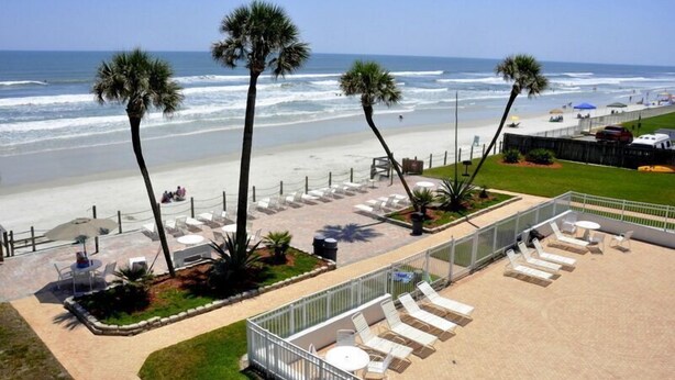 A beachside patio with sun loungers, palm trees, and a view of the ocean. - Cute 2/2!Direct Oceanfront Complex on the No Drive Beach in NSB! (New Smyrna Beach)