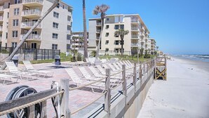 A beachfront hotel with multiple balconies, palm trees, and a sandy beach. - Cute 2/2!Direct Oceanfront Complex on the No Drive Beach in NSB! (New Smyrna Beach)