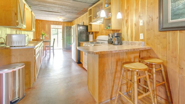 Una cocina con armarios de madera, una isla central con taburetes, un refrigerador y una cafetera.