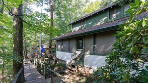 Eine Holzterrasse führt zu einem Haus, das von dichtem Baumbestand umgeben ist.