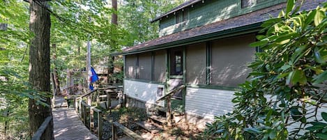 A wooden deck leading to a house surrounded by dense trees.