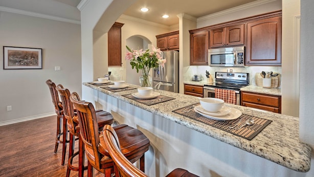 A kitchen with a long island, wooden chairs, a refrigerator, a microwave, and a sink.