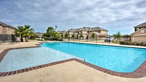 A swimming pool with a brick border, surrounded by a fence and palm trees.