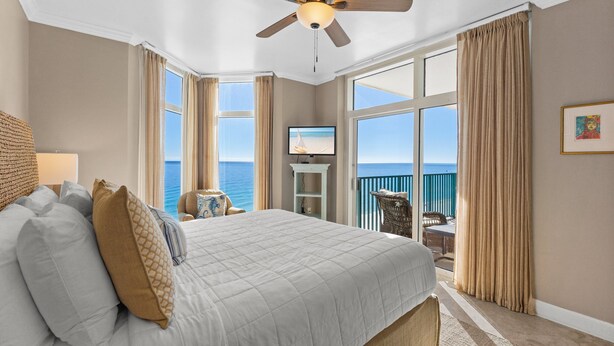 Quarto com uma cama grande, ventoinha no teto, televisão e vista para o oceano.