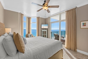 A bedroom with a large bed, a ceiling fan, a TV, and a view of the ocean.