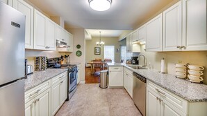 Una cocina con armarios blancos, encimeras de granito y un refrigerador de acero inoxidable, junto con una zona de comedor con una mesa y sillas.