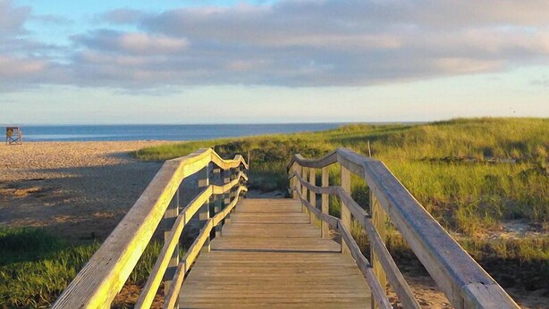 A wooden boardwalk leading to a beach with a grassy dune and a clear sky. - Close to kid-friendly Ridgevale Beach! (Chatham)