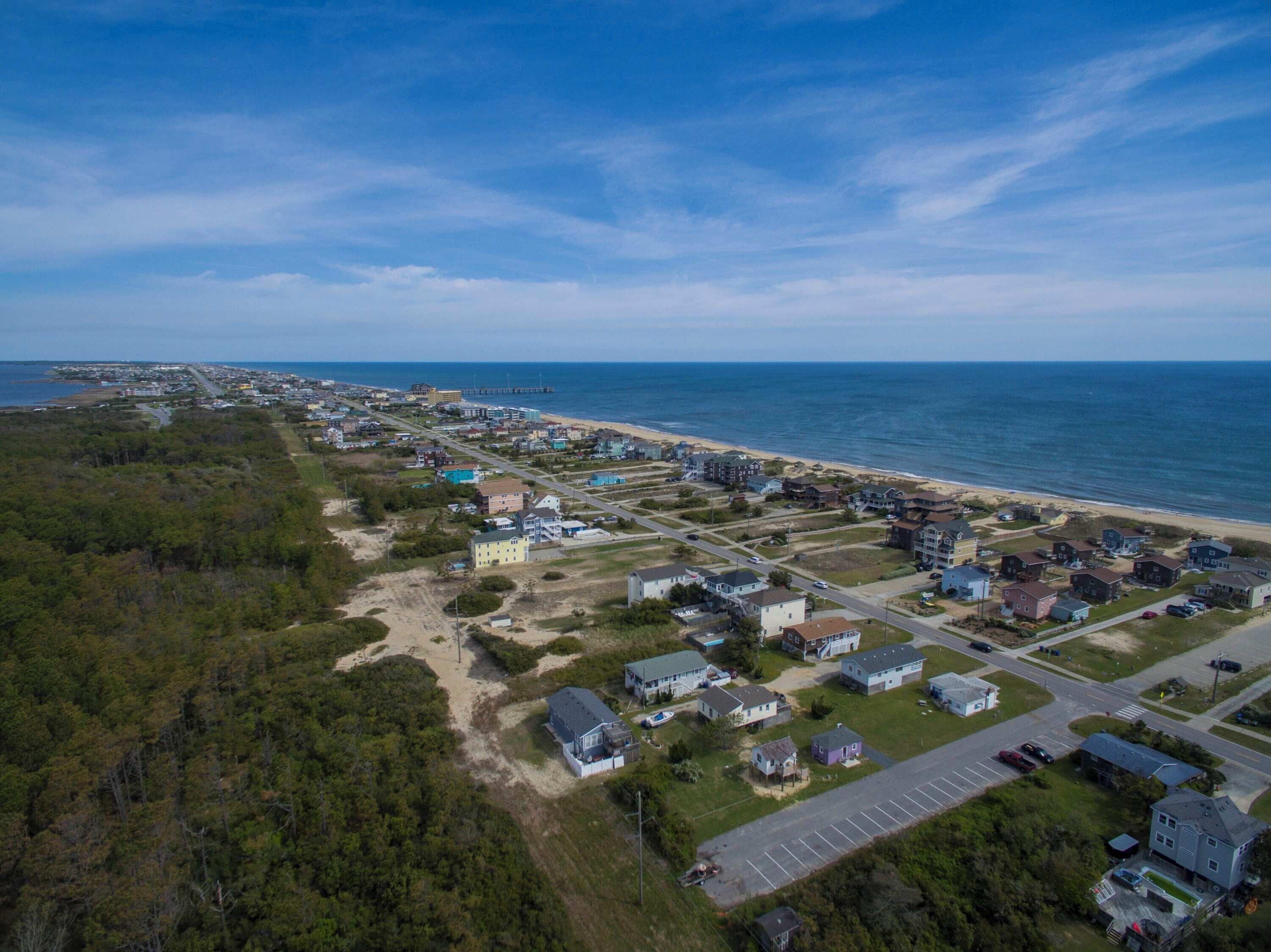 Vue aérienne d’une zone résidentielle côtière, avec des maisons, une plage et une jetée.