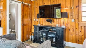 Una habitación con paredes de paneles de madera, un mueble negro para entretenimiento con un televisor, y una puerta que da al baño.