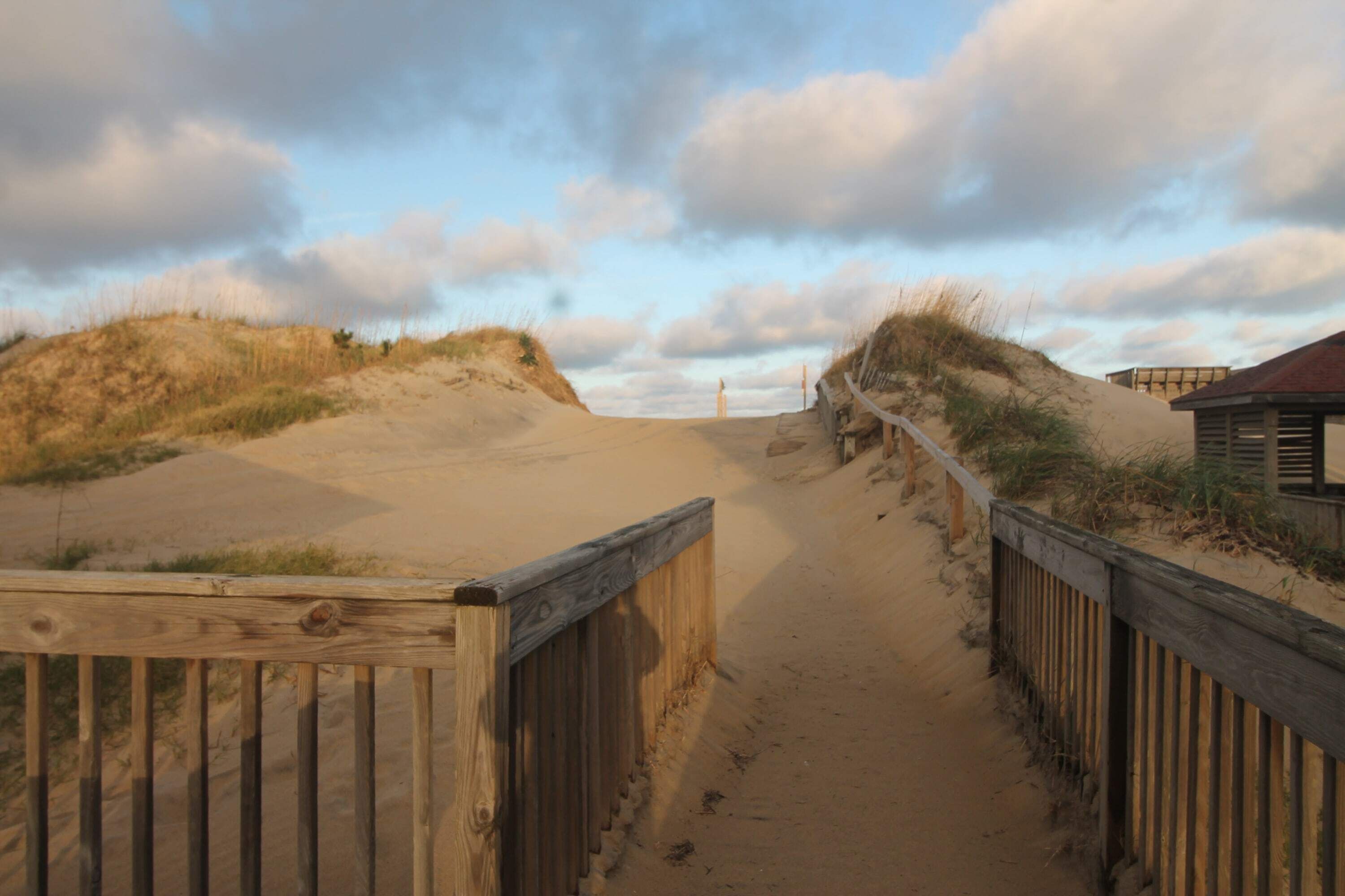 A wooden pathway leading to a beach with dunes and a wooden fence.