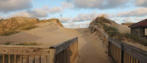 A wooden pathway leading to a beach with dunes and a wooden fence.