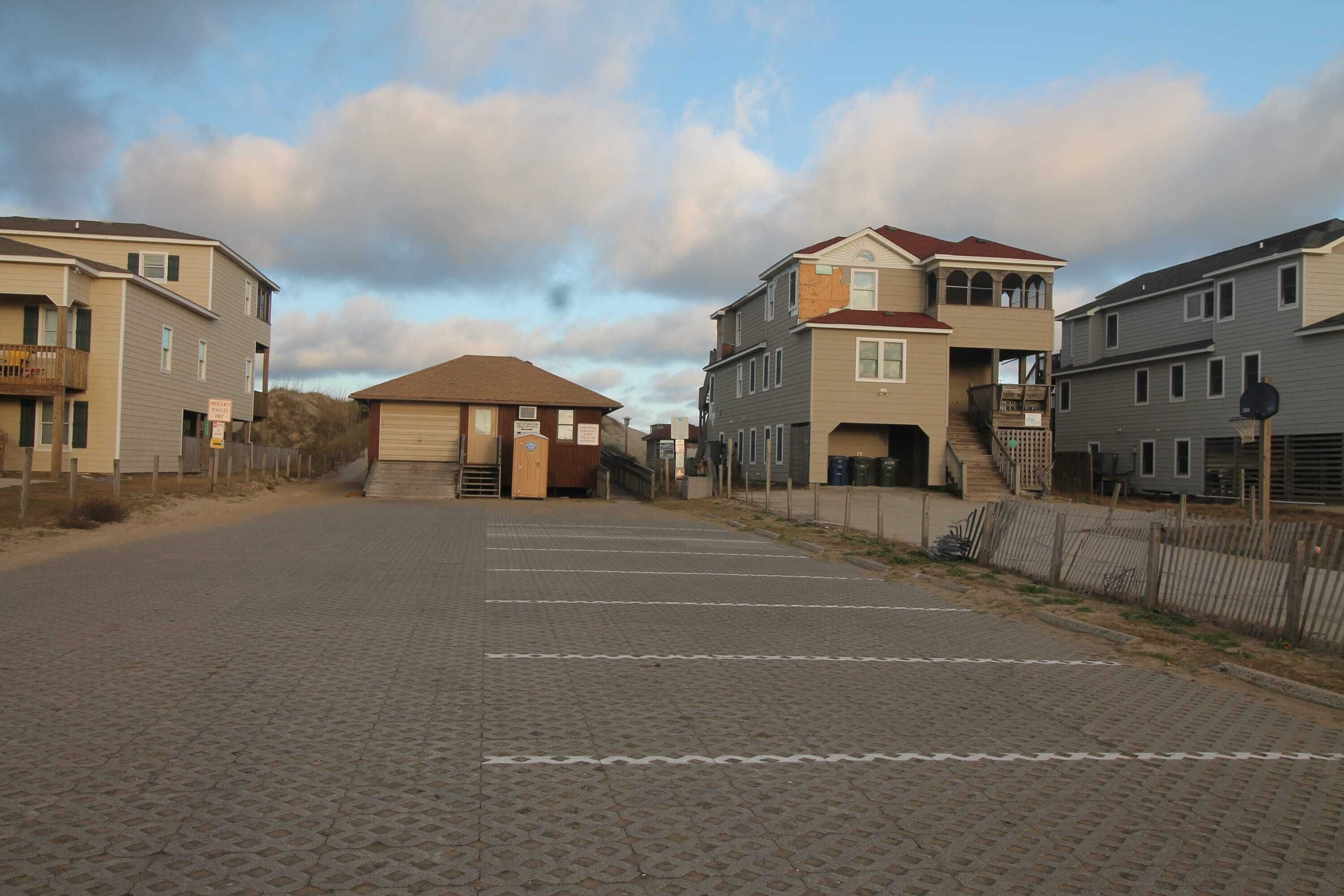 A parking lot with paved ground, a building with a brown roof, and a staircase leading to a second floor.