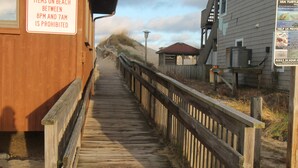 Pasarela de madera que conduce a un edificio con un letrero que prohíbe dejar objetos personales en la playa entre las 8 PM y las 7 AM.